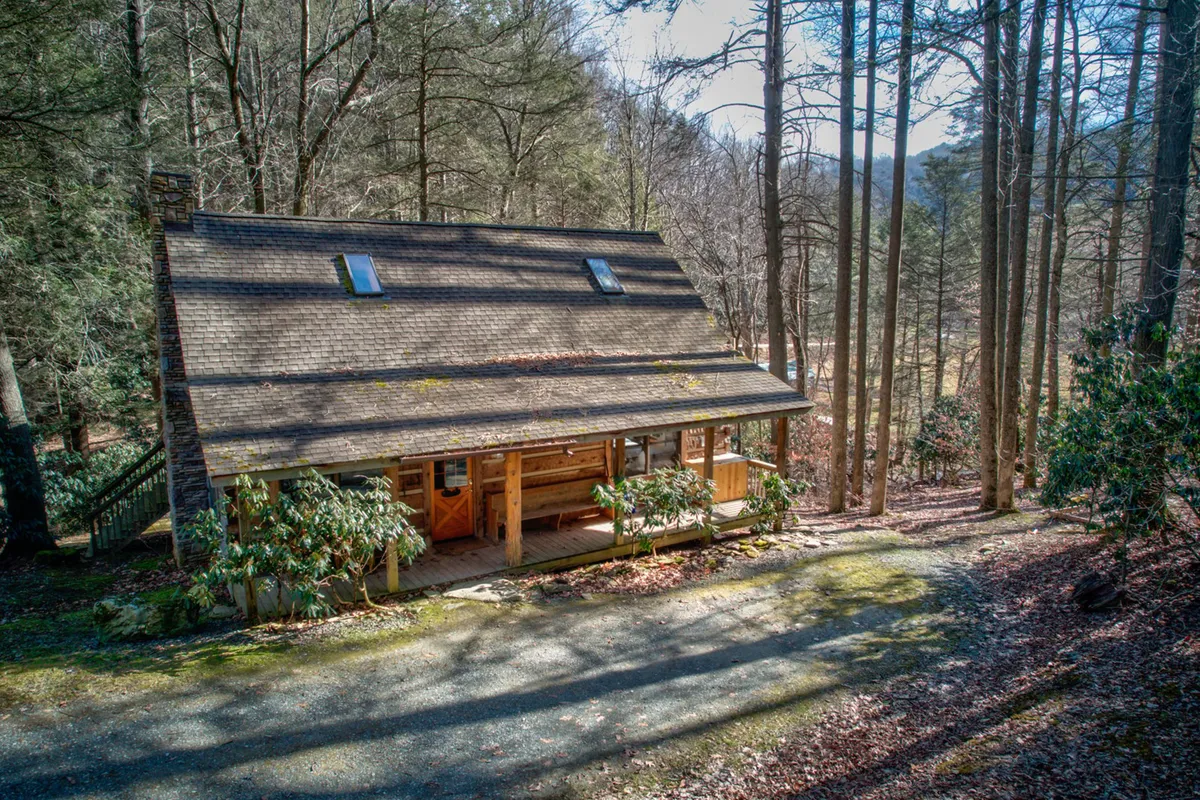 A broad wooden porch is framed by surrounding trees and a sloped roof, suggesting seclusion and immersion in nature. The peaceful setting is ideal for sunrise views or quiet evening stargazing.