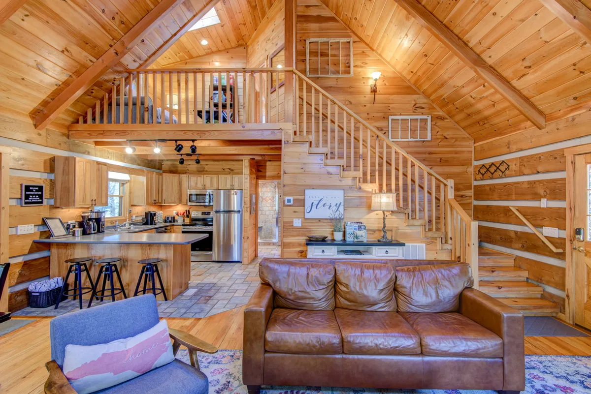 A welcoming open-concept space featuring a leather sofa, a wooden staircase, a glimpse of the inviting kitchen, and a decorative sign. The area exudes warmth, with a clear view of both the family room and kitchen, ideal for gatherings, relaxing, and cooking together.