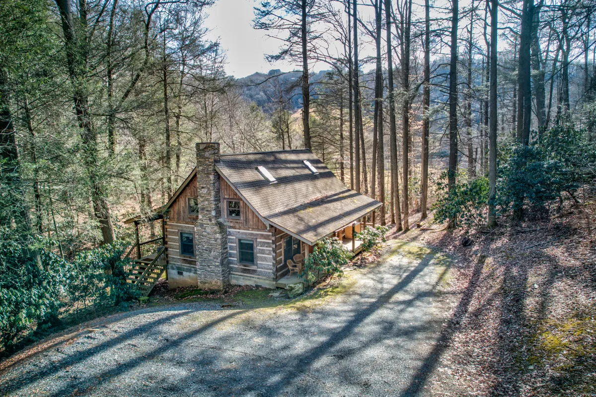 A cozy log cabin exterior with a stone chimney and a wide wooden porch set amidst lush greenery. The inviting porch is perfect for relaxing after a day of outdoor adventure, and the natural wood textures harmonize with the surrounding landscape.
