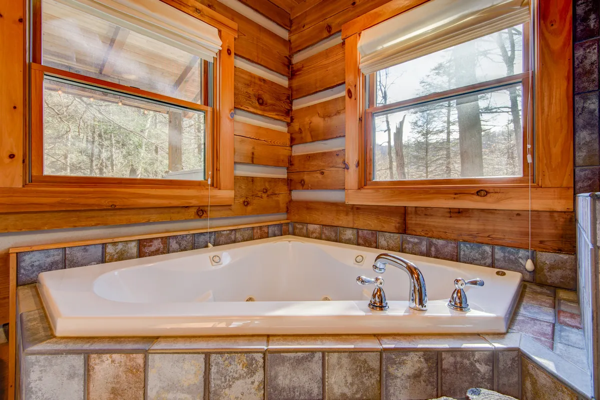 A serene interior space featuring a jacuzzi tub framed by warm wooden walls and large windows, offering a view of the outdoors and inviting in natural light. The quiet ambiance suggests ultimate relaxation after a day spent exploring outside.