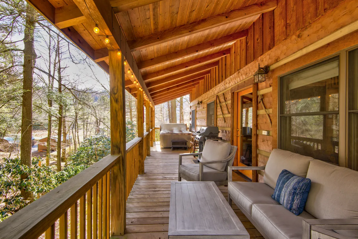 This image showcases a cozy wooden porch with comfortable seating, an outdoor grill, decorative string lights, and lush natural surroundings. The inviting setup signals a perfect spot for family barbecues, evening relaxation, and together time immersed in nature.