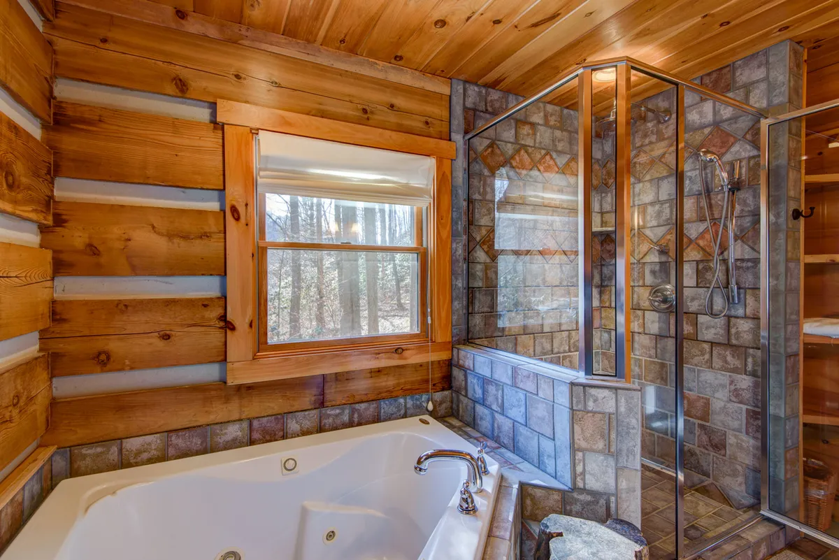 A spa-inspired bathroom with a jacuzzi tub, glass shower enclosure, wooden walls, and a large window overlooking the forest. The space exudes tranquility and invites relaxation after mountain adventures.