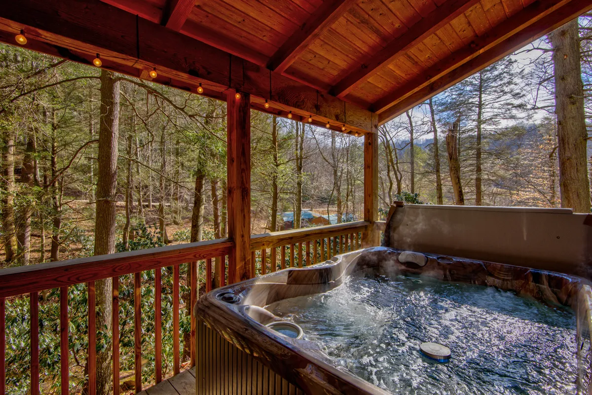 An inviting hot tub sits on a spacious wooden deck surrounded by lush trees and natural greenery. The deck is bordered by a wooden railing, and the hot tub offers clear views of the forested landscape, perfect for relaxation. The setting hints at the tranquility and immersive nature experience described in the section.