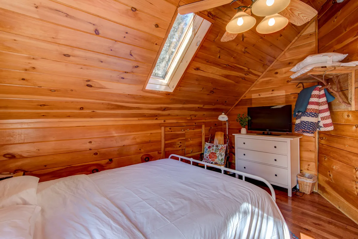 A loft space with inviting wooden walls, skylight, bed, dresser, and decorative chair. The atmosphere feels airy and flexible—ideal as an extra sleeping area or a playful hideaway for children.