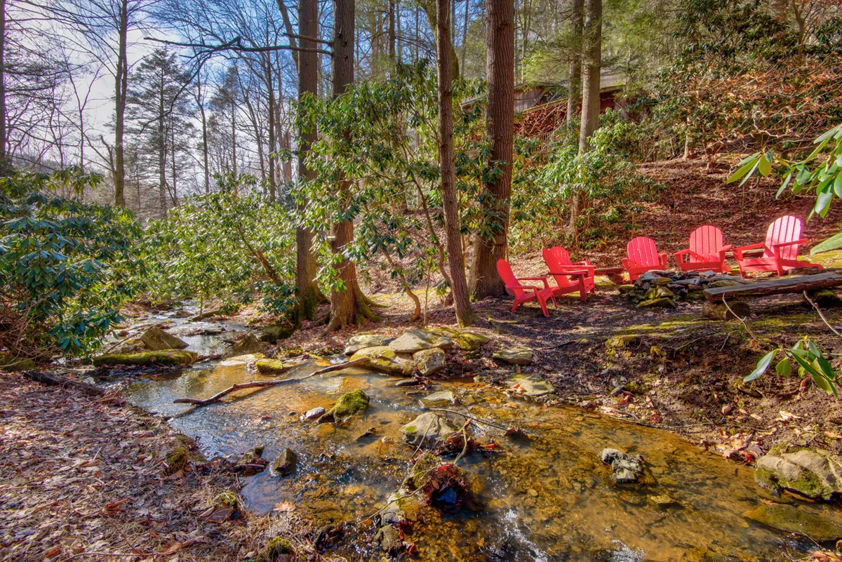 Red Adirondack chairs are set on the edge of a lively stream, nestled among lush green foliage and natural rock formations. The sense of peace and connection to water is palpable, evoking the gentle sounds of the nearby stream mentioned in the narrative.